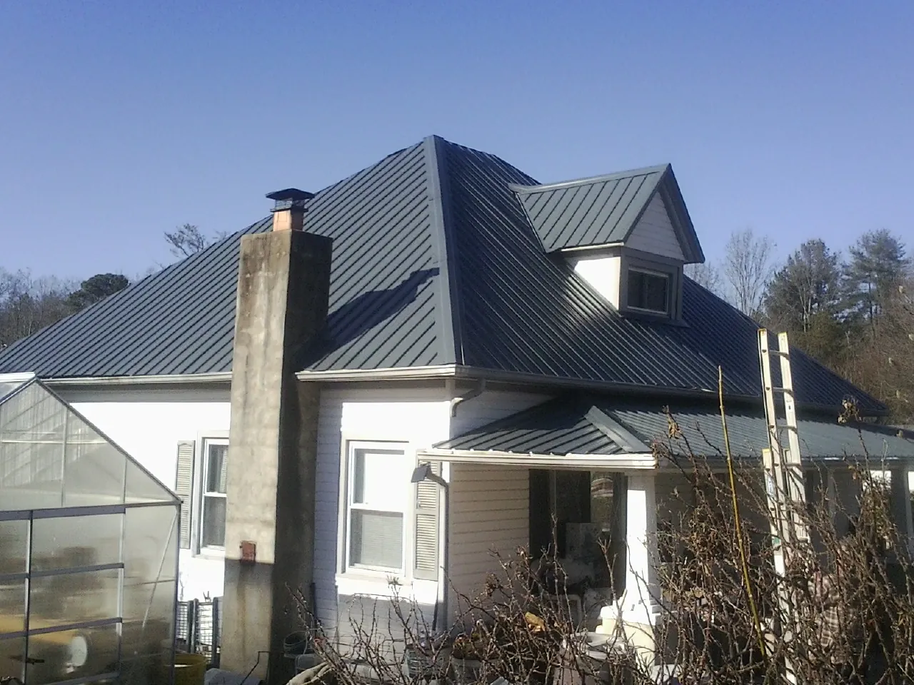 Dark blue standing seam metal roof on a white farmhouse with dormer — Slate & Tile Roof Repair by Roofing Brothers in Grain Valley