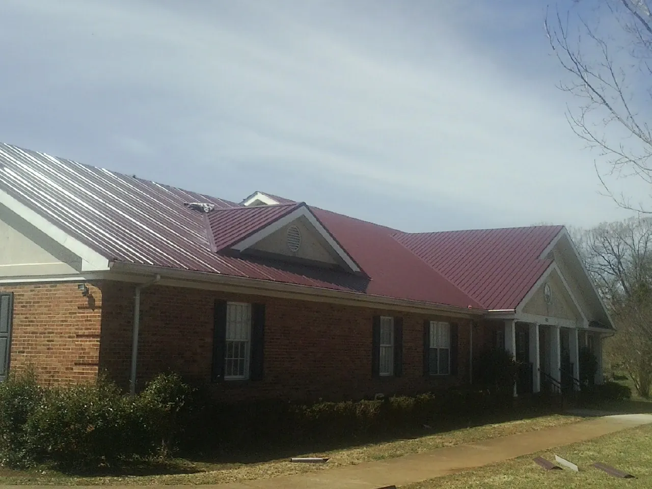 Red metal roof with gabled entries on a long brick building, from a Hail Damage Roof Repair job in Grain Valley