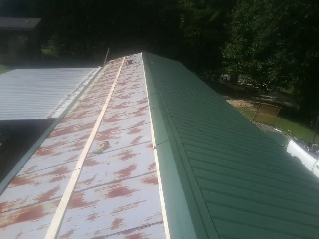 Old rusted panels beside newly installed green metal roofing — Wind Damage Roof Repair by Roofing Brothers in Grain Valley