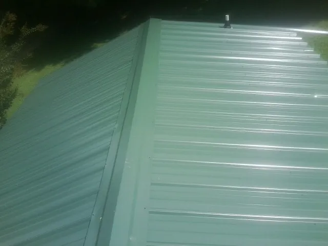 New green metal panels meeting at the ridge of a roof — Flat Roof Repair work by our crew in Grain Valley
