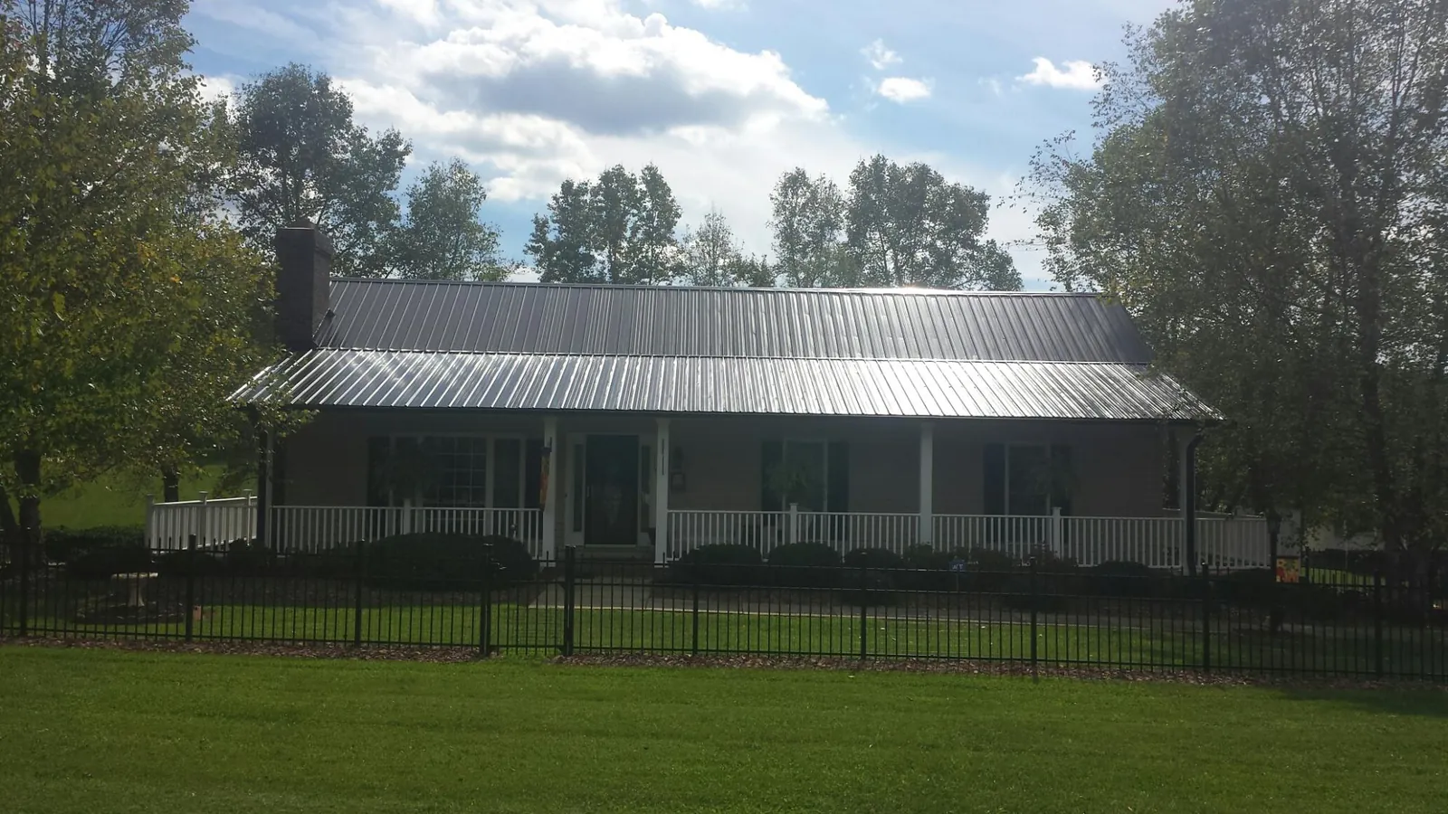 Gray metal roof on a brick ranch with a full width front porch — Gutter Guard Installation work by our crew in Grain Valley