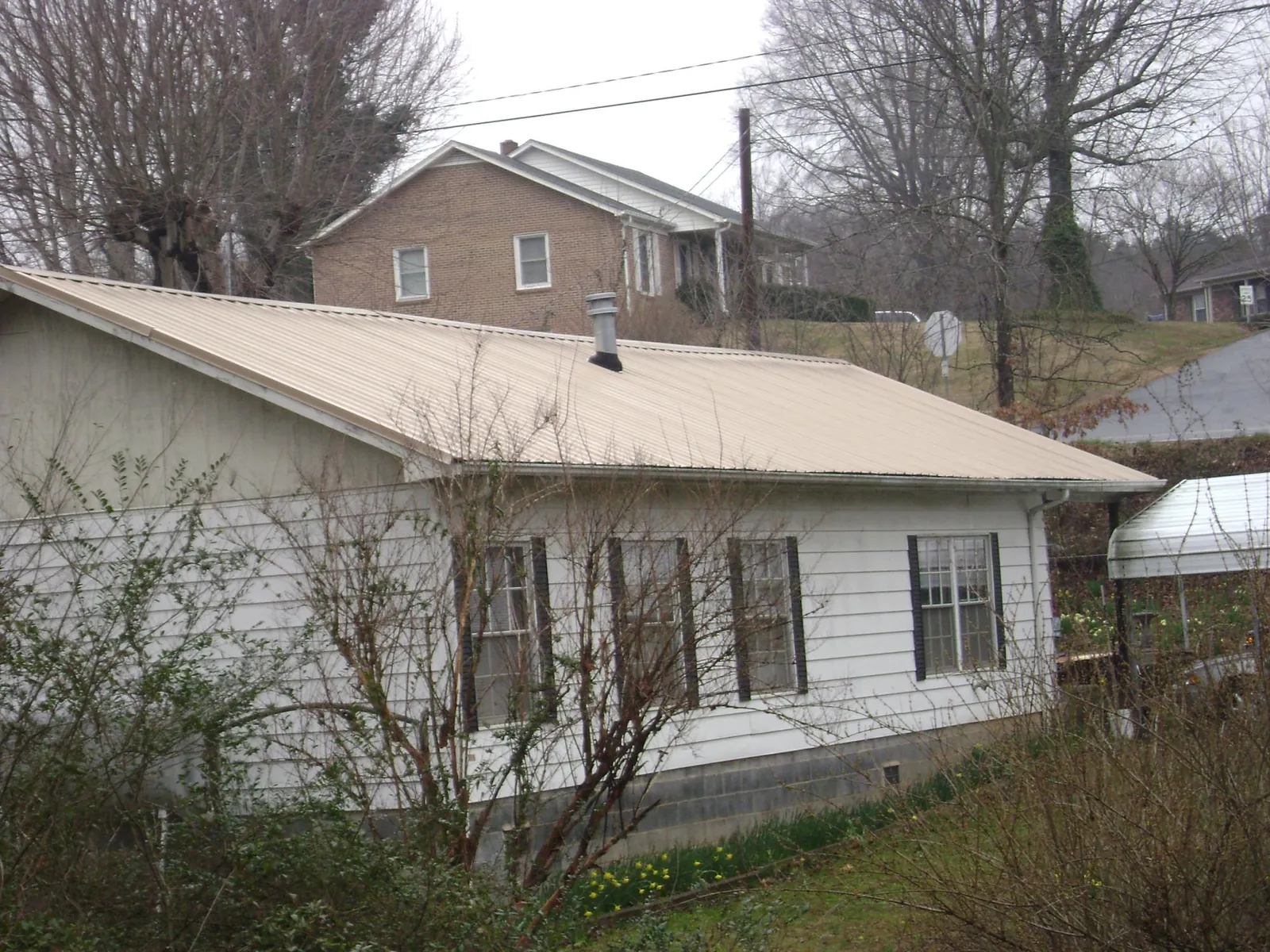 Tan metal roof on a white sided house set into a hillside — Commercial Roofing by Roofing Brothers in Grain Valley