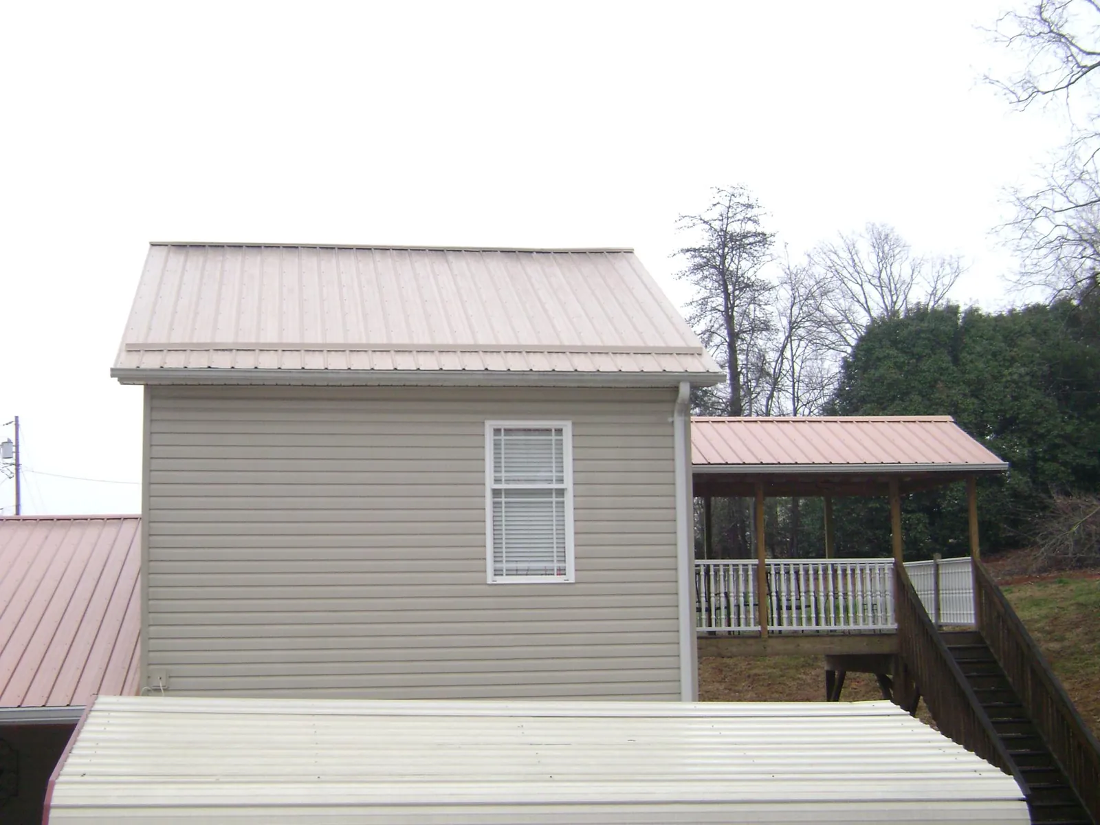 Tan metal roofs on a two story addition and attached porch, from a Roof Replacement job in Grain Valley