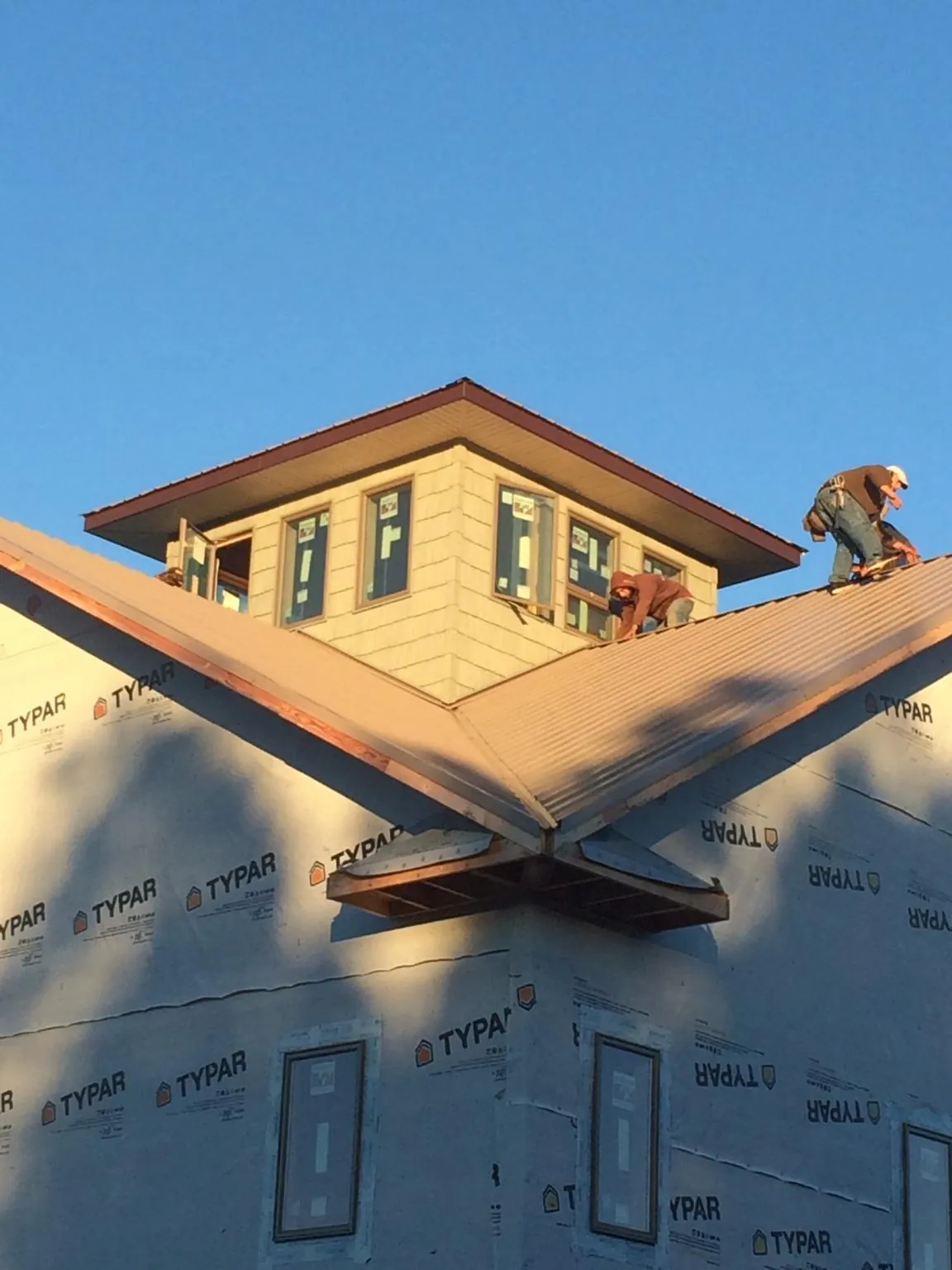 Roofers working around a rooftop cupola on a new metal roof at sunset — Roof Waterproofing in Grain Valley by Roofing Brothers